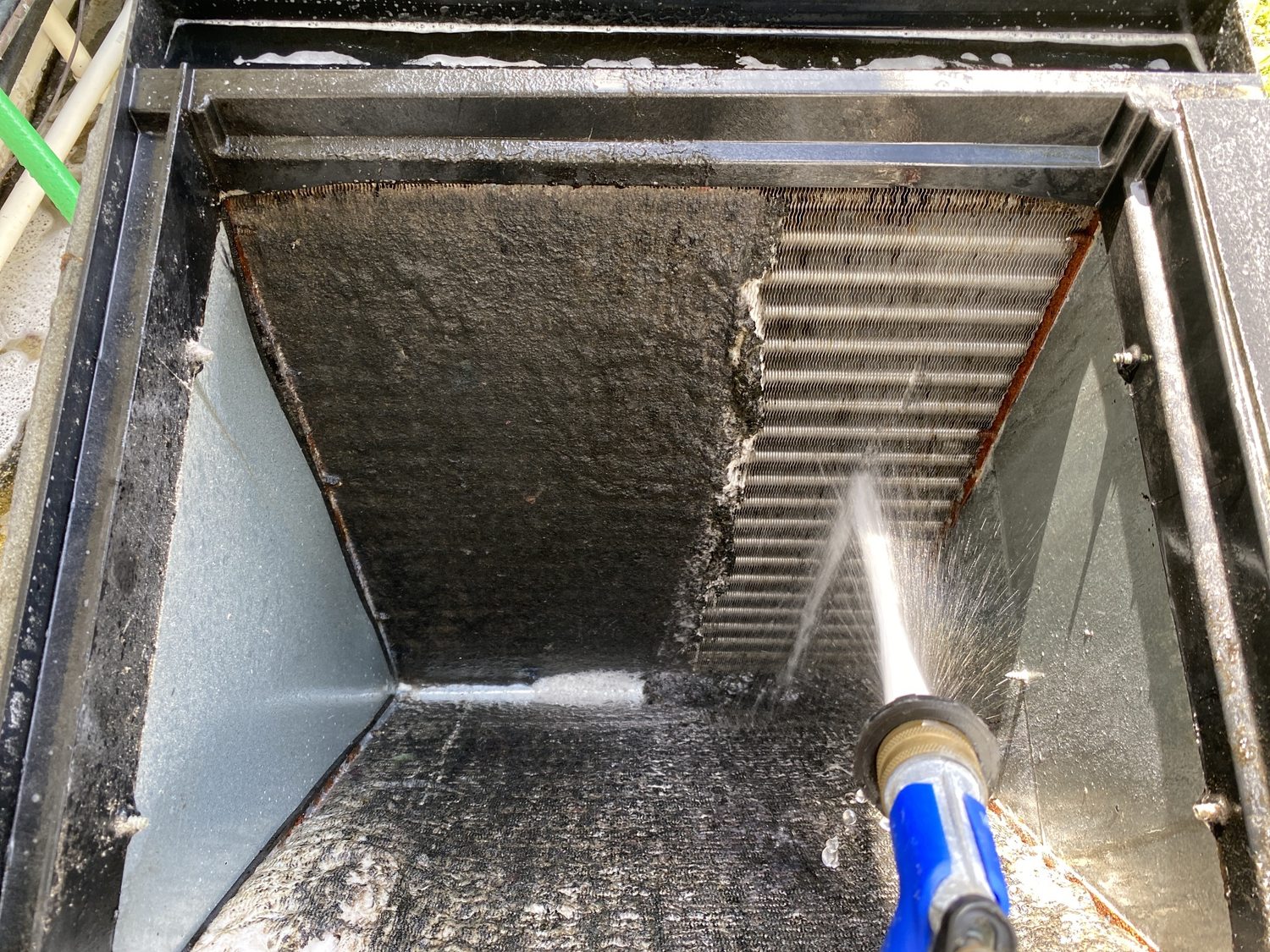 Evaporator coil mid-cleaning, dark buildup on one side and clean fins on the other.