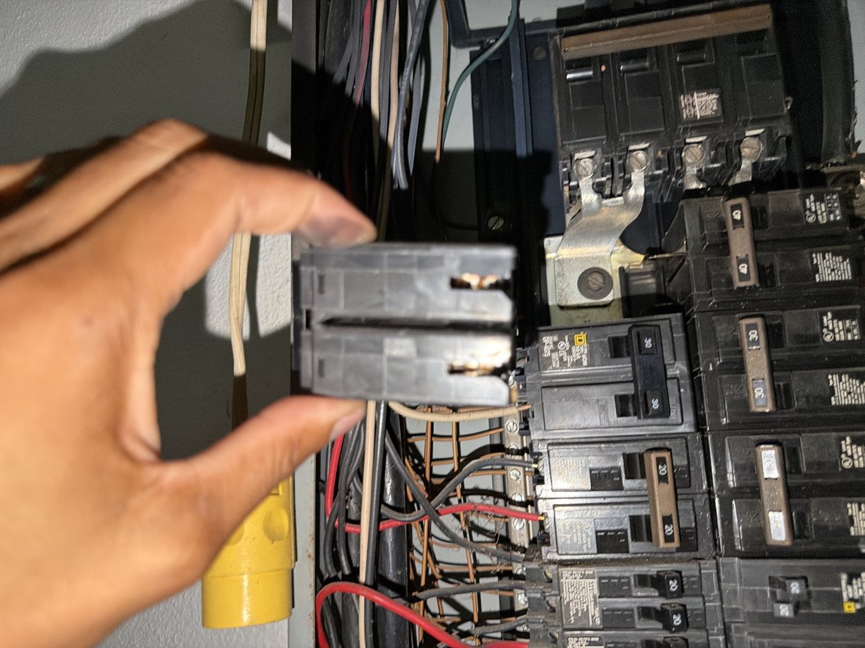 The removed breaker held in hand, showing charred contacts and melted housing.