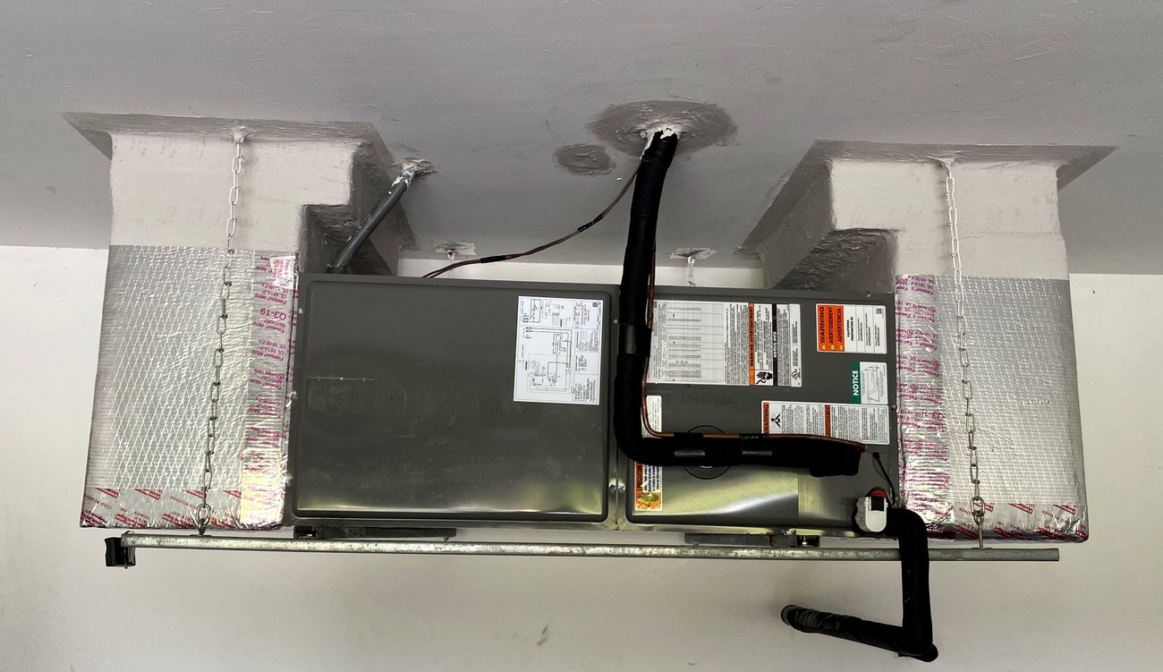 Finished ceiling air handler with insulated line set and electrical disconnect below.