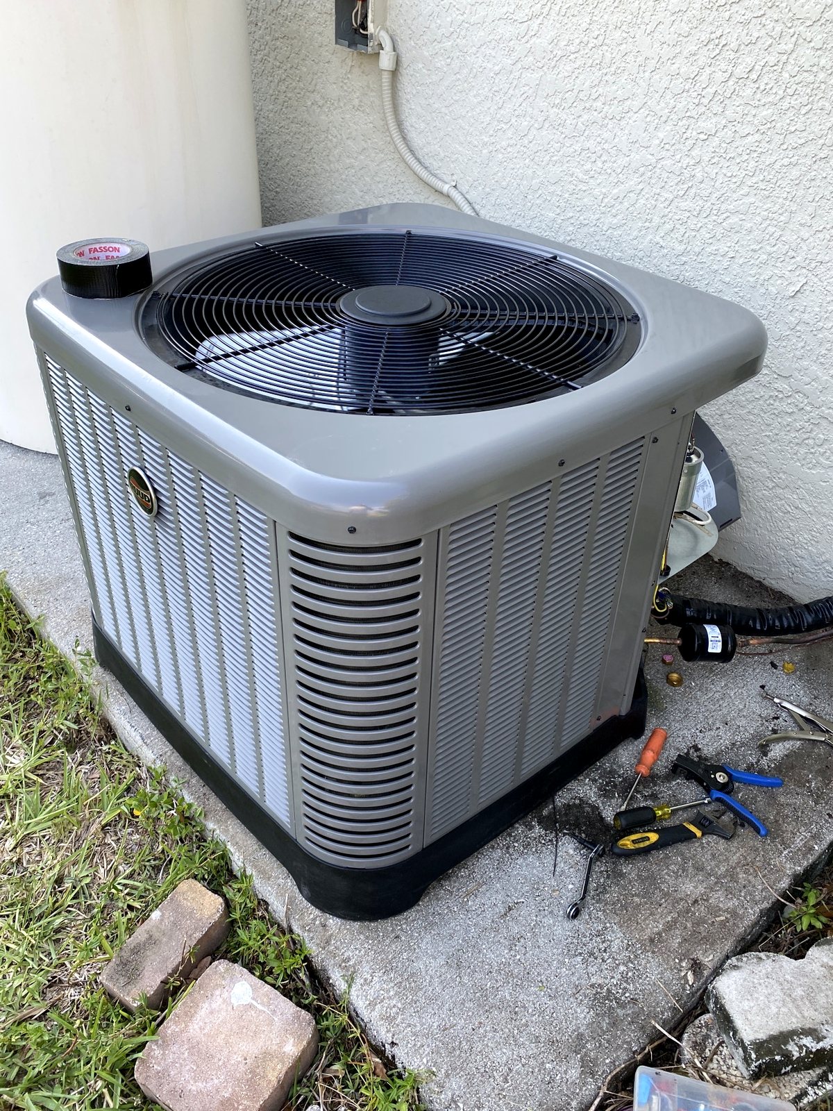 Large Ruud condensing unit anchored on a concrete pad beside a house.