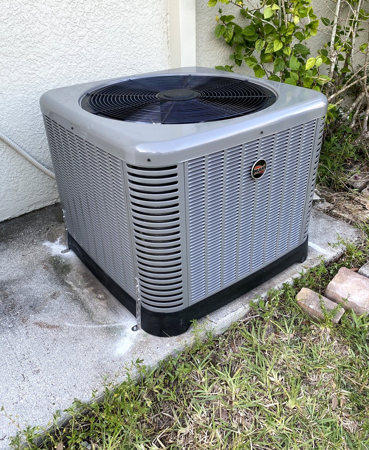 Ruud condenser set on a pad with the refrigerant line set insulated and sealed at the wall.