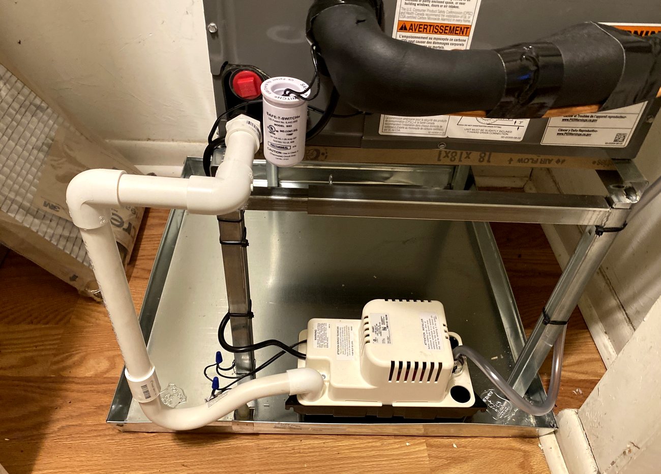 Condensate pump and PVC drain line installed in a pan beneath an air handler, with a float safety switch above.