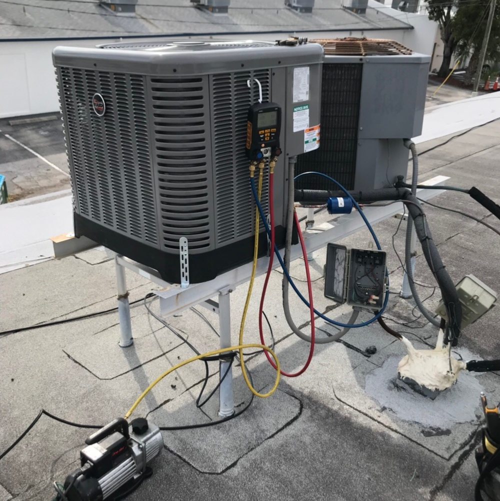 Digital manifold gauges and a vacuum pump connected to a rooftop condensing unit.