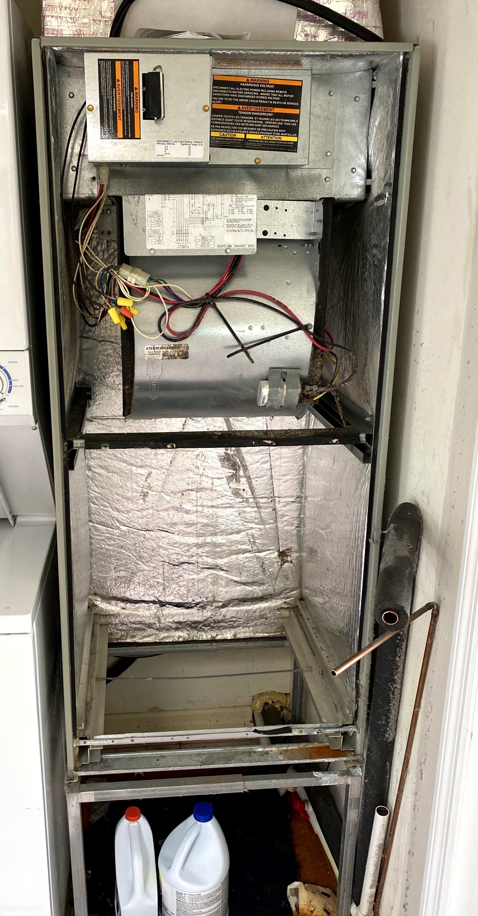 Air handler cabinet with the coil removed, showing the cut copper line stub and the empty coil compartment.