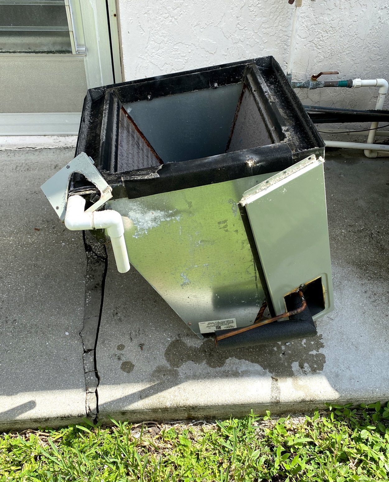 The evaporator coil out of the cabinet and sitting on concrete, cut copper lines and metering device visible on top.