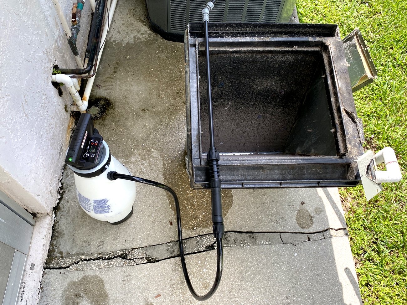 The removed coil set up outside with a battery chemical sprayer and rinse wand staged beside it.