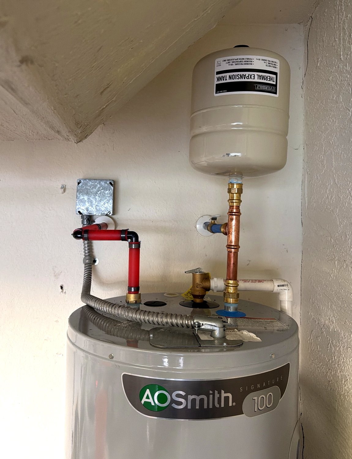 Water heater connected with red and blue PEX lines and a thermal expansion tank above.
